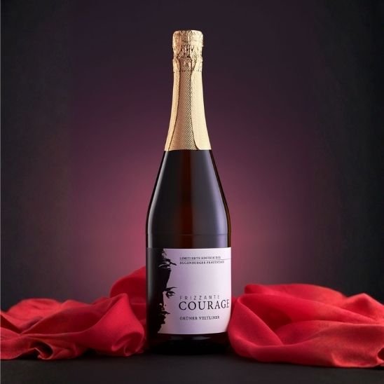 Flasche des Courage Frizzante Grüner Veltliner der Frauentage Eggenburg, elegant inszeniert mit dunklem Hintergrund und rotem Tuch
